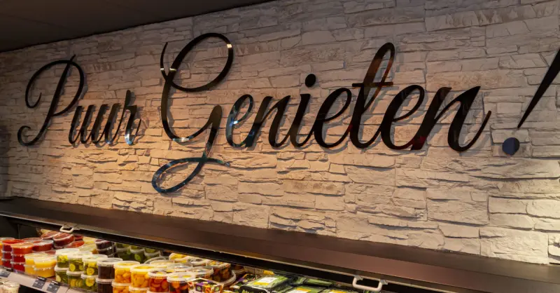 Witte stenen wand in de winkel met de tekst Puur Genieten in zwarte sierletters